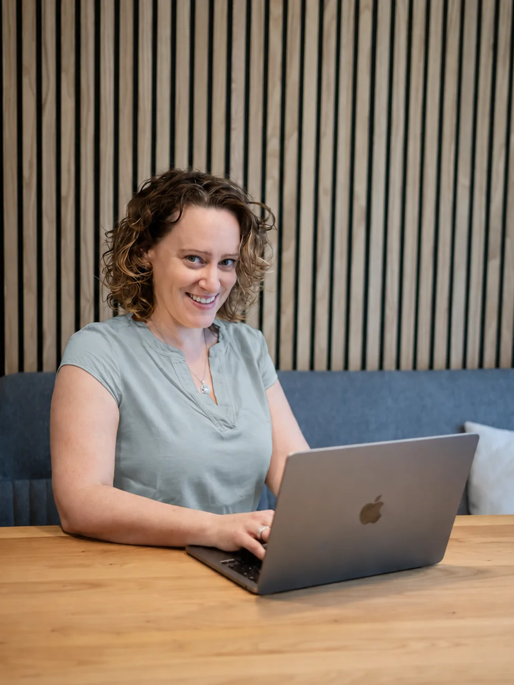 Kerstin Piez sitzt an einem Holztisch am Laptop und schaut lächelnd in die Kamera.